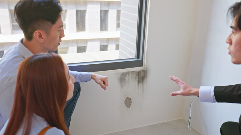 close-up of agent and home buyer inspect interior wall damage near window showing seepage cracks and mold during home sale discussion in bare house