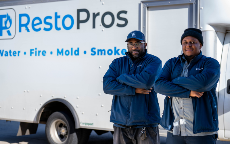 Two restopros employees stand with arms crossed in front of a truck