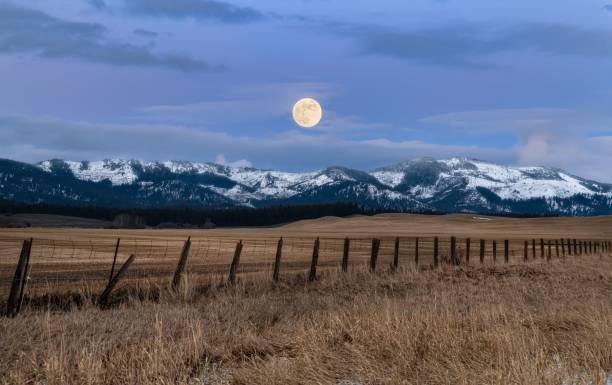 A wooden fence situated next to a majestic mountain range illuminated by a full moon in Idaho