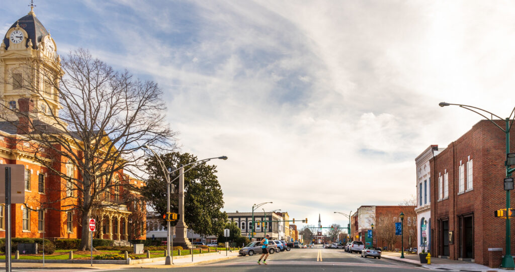 Monroe, NC, USA-28 Jan 2023: Wide angle view down Main Street past Court House toward First Baptist Church. Sunny winter day. Runner crossing street.