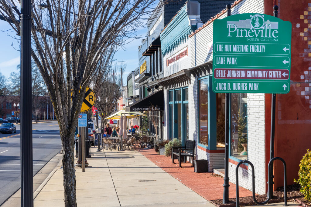 Pineville, NC, USA-15 January 2023: A view down Main Street sidewalk, with sidewalk diners at Margaux's an Christie's on Main. Sunny, blue sky day. Directional sign to important locations in town.
