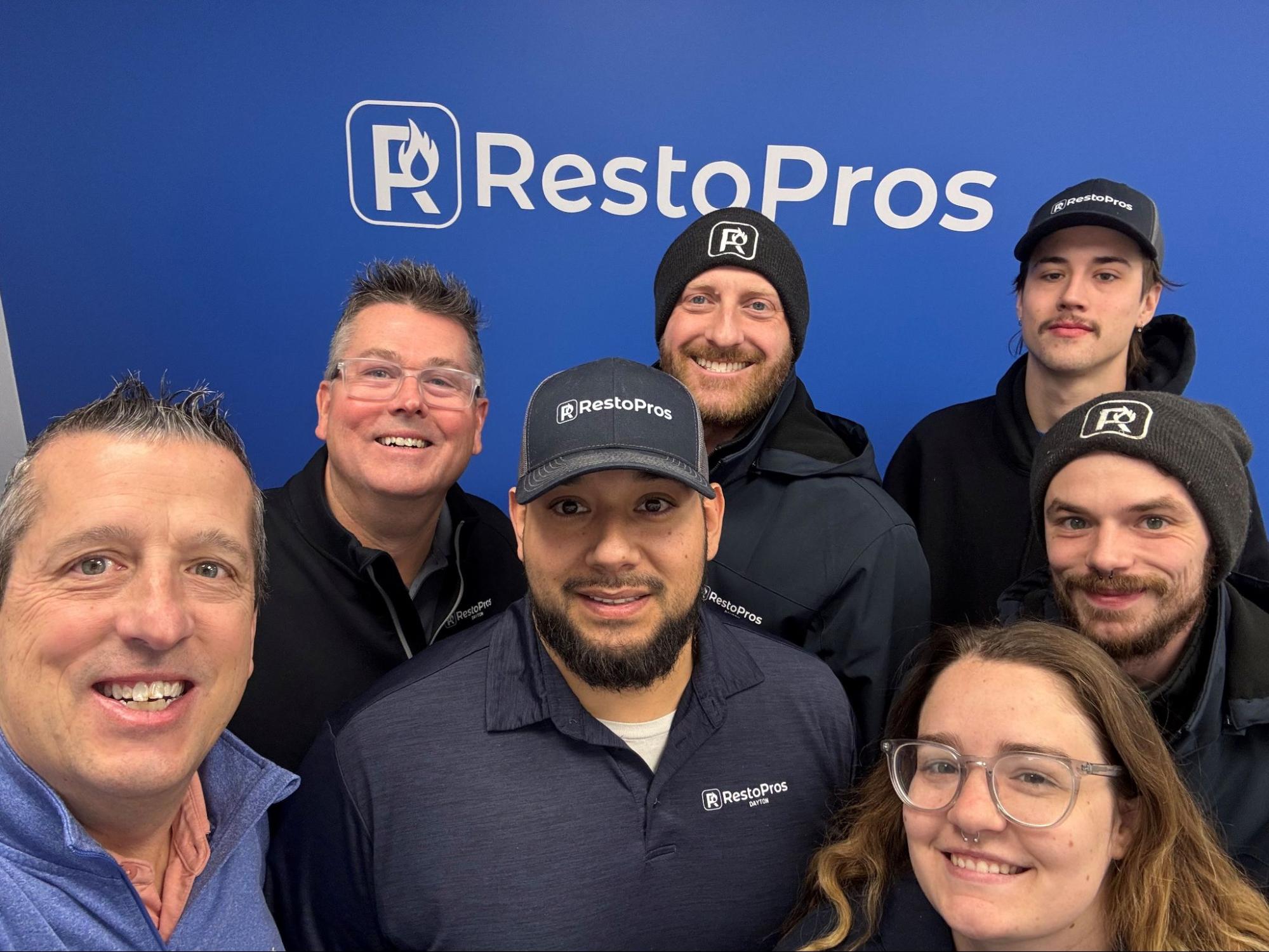 Dayton RestoPros team taking a selfie in front of a blue wall with the RetoPros logo.