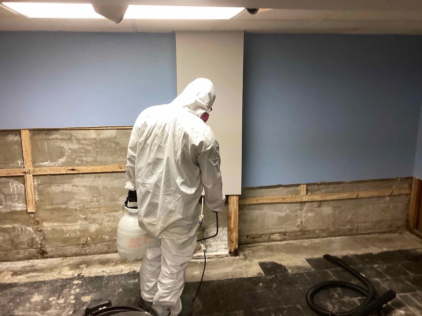 Worker in hazmat suit spraying solution onto floor