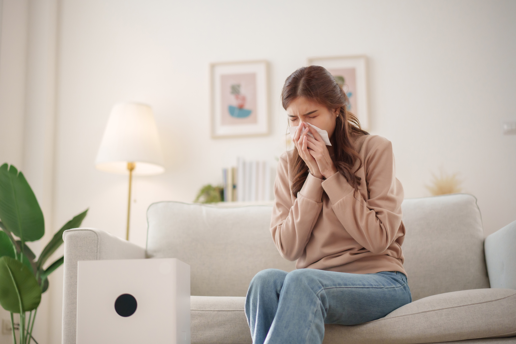Young woman experiencing allergies at home with an air purifier in a bright, cozy living room