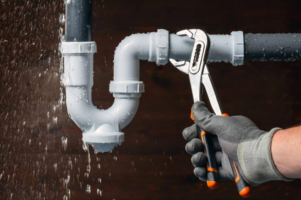 hand with wrench fixing a leaky pipe